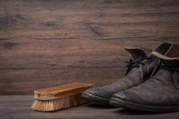 Old worn out brown leather shoes with brush over the dark background