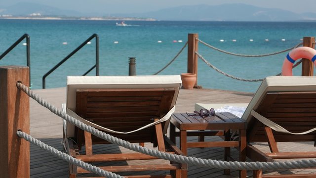 View of the emty wooden sunbeds and coffee table with a sunglasses with sea and moving boat on the background. 4k