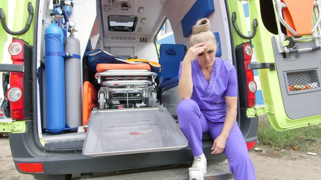 Emergency medical service upset tired paramedic sitting in front of ambulance, jib crane shot