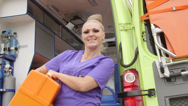 Emergency medical service cheerful female paramedic with life support kit in front of ambulance