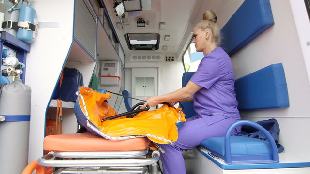  Emergency medical service female paramedic working at the site of illness or injury inside of ambulance preparing inflatable immobilizer and stretcher for patient transportation