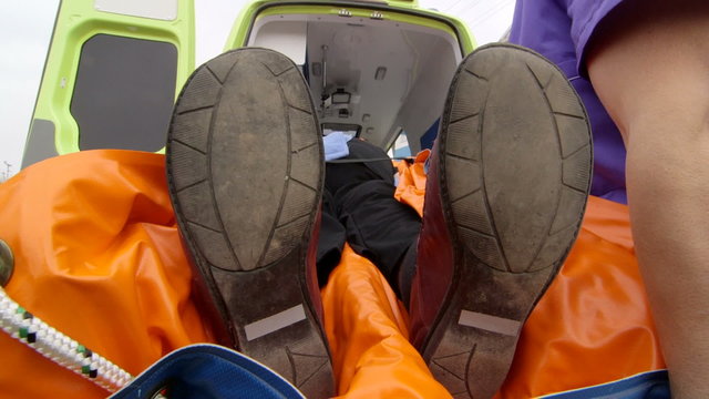 Emergency medical technicians and paramedics loading sick or injured senior patient into an ambulance, staff point of view