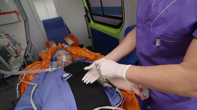 EMT paramedic wearing latex gloves provide medical care to senior patient in ambulance preparing an intravenous infusion during transportation to hospital