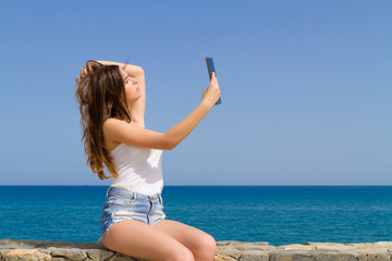 Beautiful teenage brunette teen in jean shorts using a tablet.