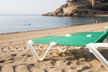 Fototapeta na wymiar Chaise-Loungers on deserted beach in Tossa De Mar, Spain.