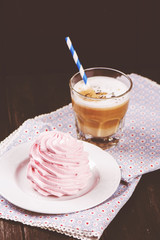 Coffee latte with crunchy pink meringue over black wooden background. Tasty breakfast concept. Selective focus, toned image