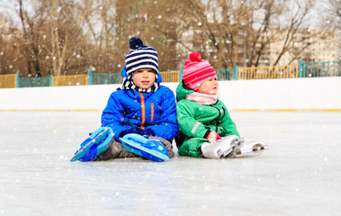 little boy and girl sitting on ice with skates