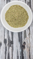 Dried oregano herbs in white bowl over wooden background