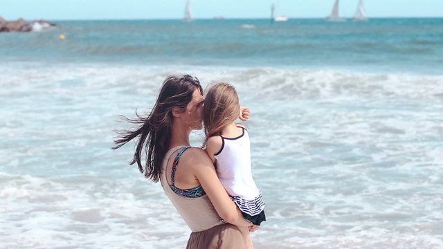 Mother and daughter hug kissing on the sea beach