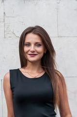 Portrait of a Smiling Happy Elegant Young Woman in Black Dress Standing Against Blue Wall Background