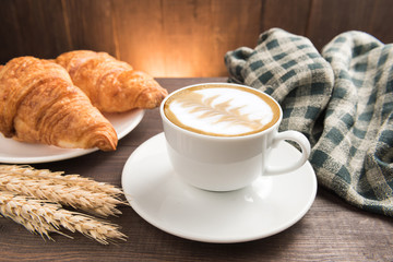 Breakfast coffee cup and croissant on wooden table