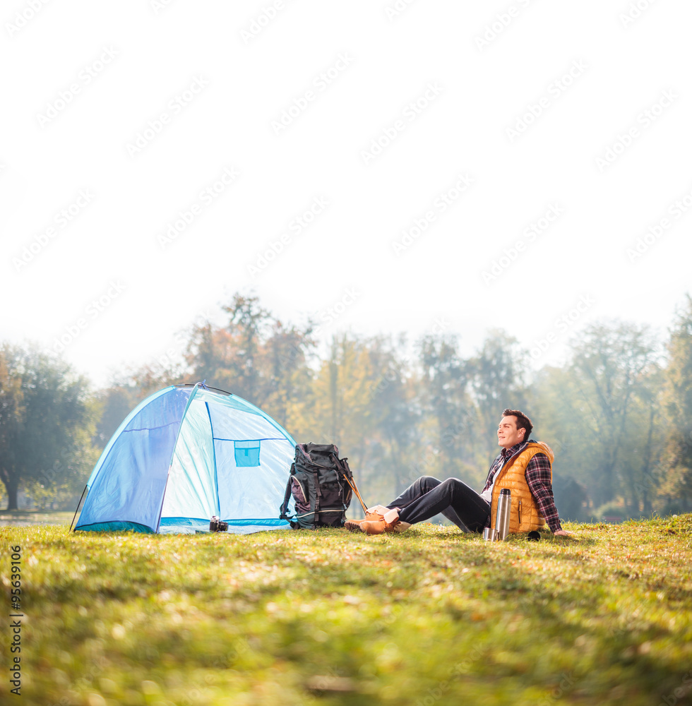 Wall mural Relaxed hiker sitting next to a blue tent