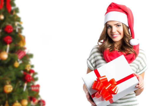 Pretty girl in Santa hats holding a gift box on the background of the Christmas tree.
