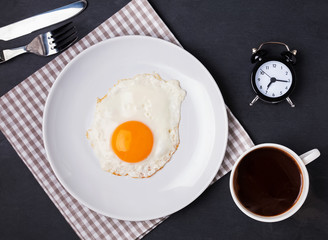 Fried egg on the plate, cup of coffee and clock, morning concept