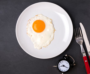 Fried egg on the plate, fork, knife and alarm clock