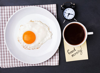 Fried egg, coffee and alarm clock on the black background