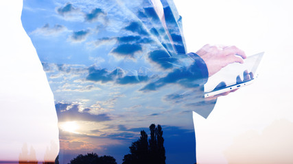 Double exposure of buisnessman with tablet and sunrise clouds background