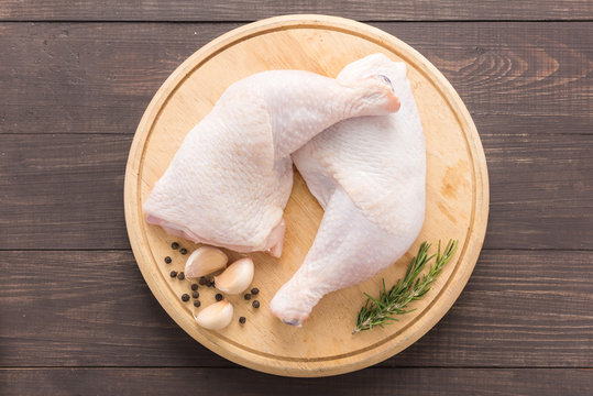 Raw chicken leg on cutting board on wooden background