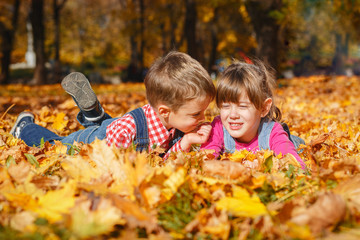 Brother and sister enjoying the autumn sun lying on yellow leaves