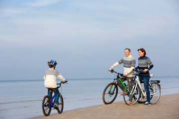 Naklejka premium Young family of three riding bicycles on beach