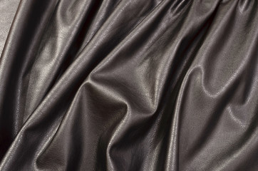 Close up on crumpled black leather material textured fabric. Shiny black pleather as a background.