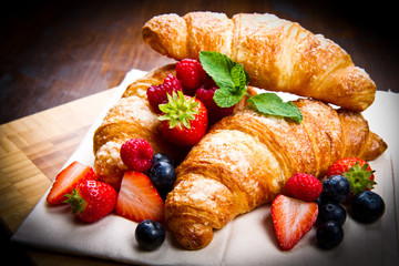 Fresh tasty croissants with berries on wooden background