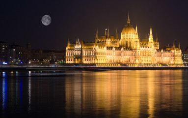 Fototapeta premium Budapest at night, Parliament building reflected in Danube river, full moon on sky