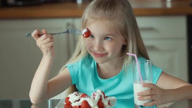 Closeup portrait of a girl eating strawberries with cream and drinking milk and looking at camera