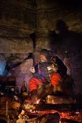 Old medieval King in armor with dish is sitting on furs near the