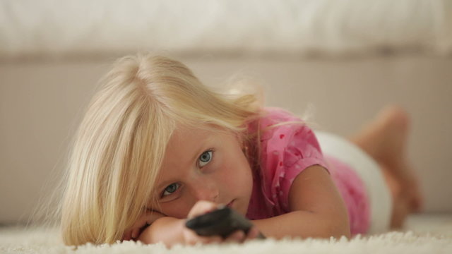 Beautiful little girl lying on carpet using remote control and smiling
