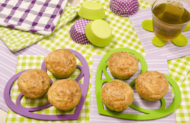 Close up on delicious muffins on heart shape holder. Cup a tea and muffins on colorful napkin.