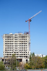 Fototapeta na wymiar Big hoisting tower crane and top section of modern construction building in a city over cloudless sky