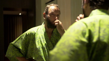 Young man in bathrobe brushing his teeth in bathroom

