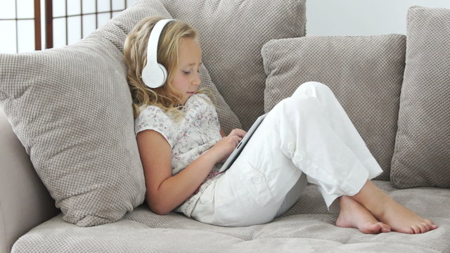 Girl resting on the couch with a tablet pc and listens to music