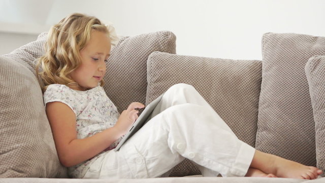Girl sitting on couch with tablet pc and smiling