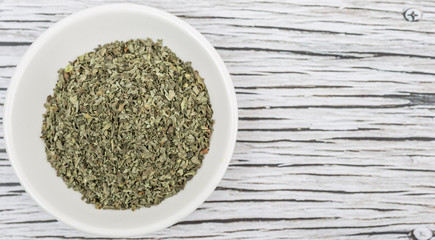 Dried basil leaves herbs over in white bowl over wooden background
