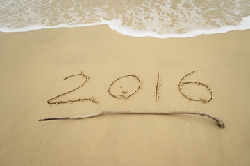 Year 2016 hand written on the white sand in front of the sea