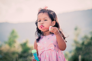 Child cute little girl blowing a soap bubbles in the park