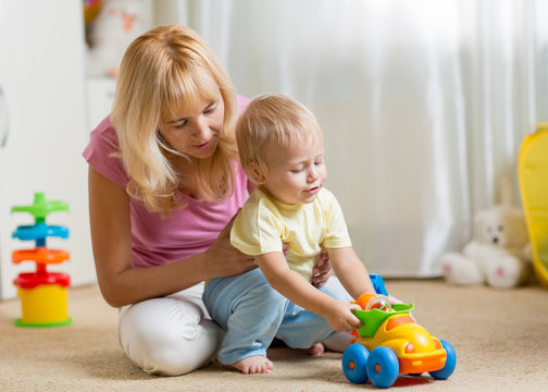 Mother and child son play with toy car on nursery floor