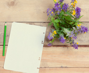 bouquet of wild flowers and a piece of paper with a pencil on a wooden table.view from above. toned.great blank for your design