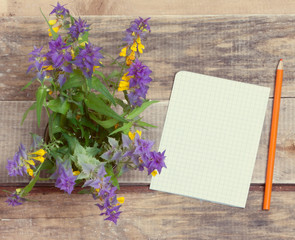bouquet of wild flowers and a piece of paper with a pencil on a wooden table.
view from above. toned.great blank for your design