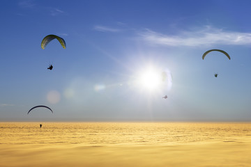 Four paragliders over a sea of clouds with sun