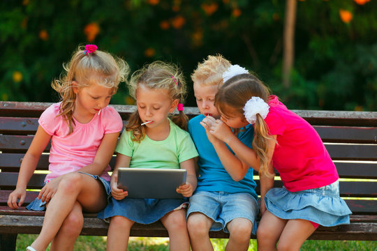 Preschool Children are sitting on a bench at the park