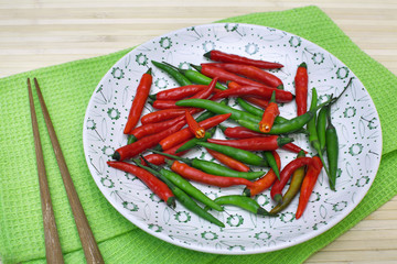 Decorative composition with chili pepper on a plate and chopsticks on table-napkin over bamboo background. Image of natural materials. Eco style.