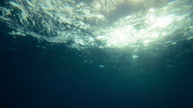 Beautiful underwater sea scene view with natural light rays in slow motion, shining through the water's glittering and moving surface, caustics, bubbles, and foam, perfect  and digital composition
