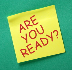 The question Are You Ready in red text on a yellow sticky note attached to a green notice board as a reminder