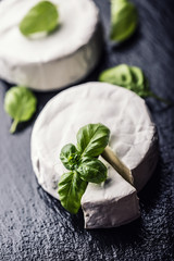 Brie cheese. Camembert cheese. Fresh Brie cheese and a slice on a granite board with basil leaves four colors peper and chili pepers. Italian and Mediterranean ingredients.