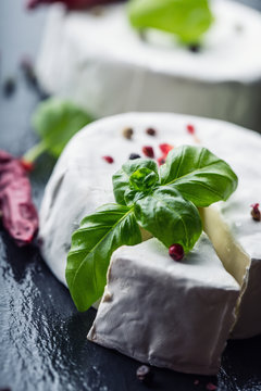 Brie cheese. Camembert cheese. Fresh Brie cheese and a slice on a granite board with basil leaves four colors peper and chili pepers. Italian and Mediterranean ingredients.