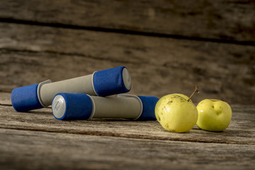 Two workout dumbbells and three fresh ripe apples lying on a tex