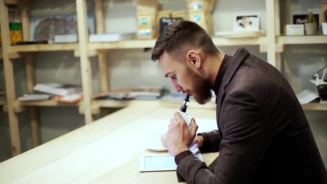 businessman in a suit reading on tablet with an e-cigarette vape